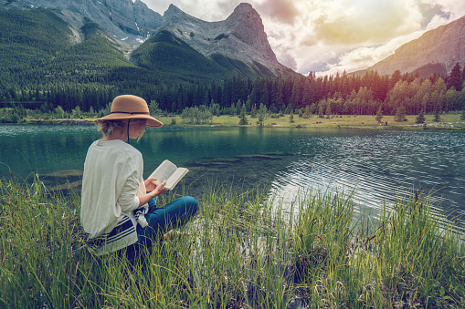 One female enjoying relaxing and reading book by a mountain lake in Alberta, Canada