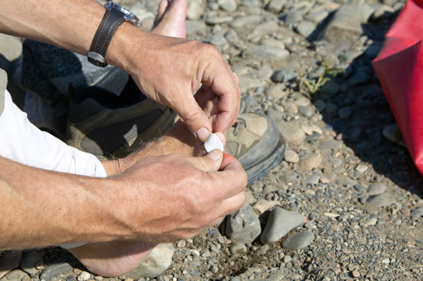Man putting a sticking plaster on his toe Man putting a sticking plaster on his toe to treat a blister caused by his hiking boots or other small injury in a close up view of his hands earth first aid stock pictures, royalty-free photos & images