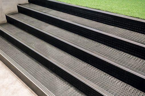 Non-slip stairs with dot pattern close up for background. Artificial grass lawn floor across with black rubber stairs.