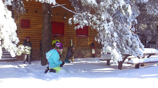 Four friends are on vacation on the mountain. They are outside, near their cottage, having fun in snow. Two of them are standing and looking at other two who are fighting with snowballs. Blonde girl is trying to fight back, but bearded guy doesn't care that she is woman. In one moment he stands up, and start shaking snow of himself, and blonde girl is looking at the camera. Leaning on the cottage two friends are cheering to them.