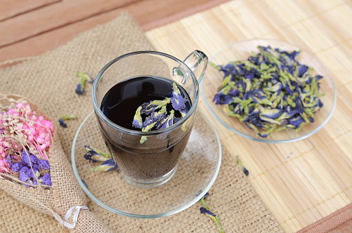 Juice of Butterfly pea in glass on wooden table with dried pea flowers. Herb drink.