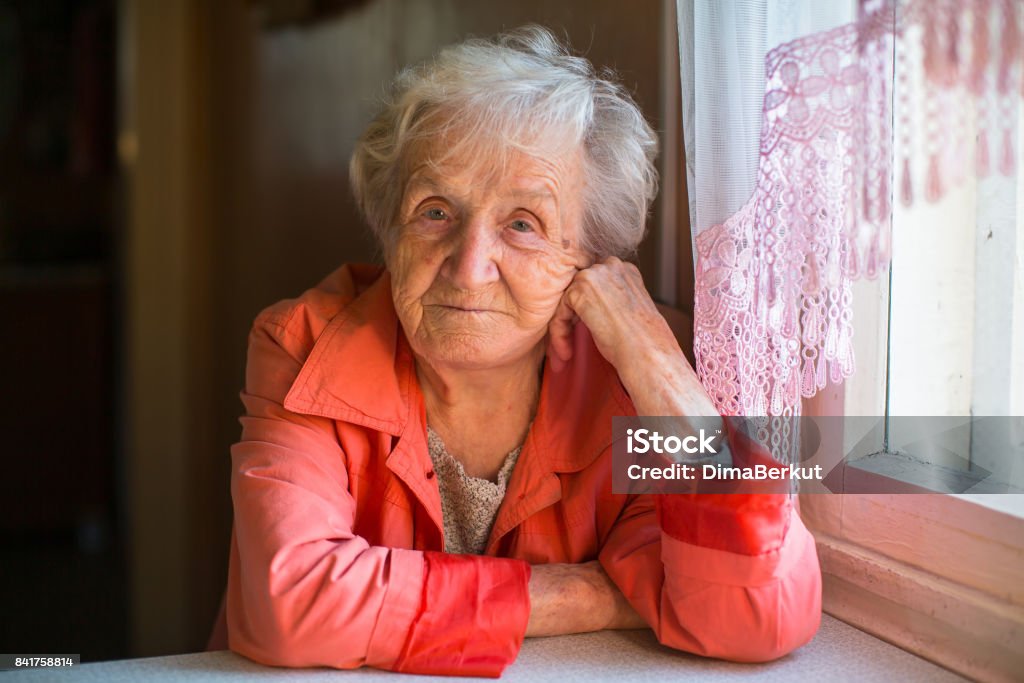 Femme âgée en veste rouge, assis à la table dans la maison. - Photo de Pauvreté libre de droits