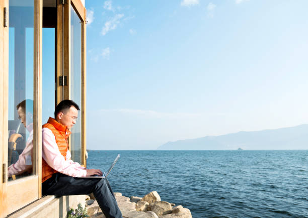 Young man working on his laptop while sitting by the lake.