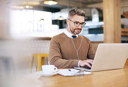 Shot of a mature man using a laptop and earphones in a coffee shop