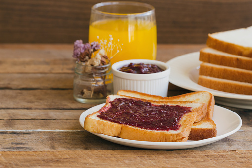 Toast bread with homemade strawberry jam served with orange juice. Homemade toast bread with jam  on wood table for breakfast. Delicious toast bread with homemade strawberry jam ready to served.