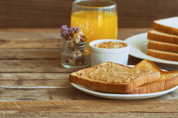 Toast bread with homemade peanut butter served with orange juice. Homemade toast bread with peanut butter on wood table for breakfast.Delicious toast bread with homemade peanut butter ready to served.