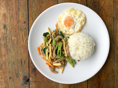 mixed vegetable stire-fried with meat and fried egg with rice in white dish on wooden background. Thai Food for health.