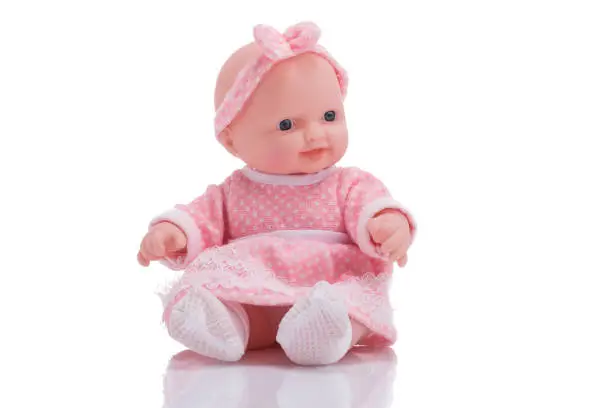 Cute little plastic baby doll with blue eyes sitting on empty background