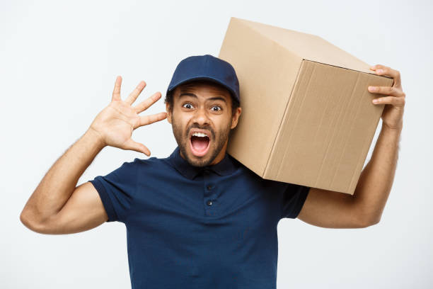 delivery concept - portrait of serious african american delivery man showing silly aggressive expression with holding a box package. isolated on grey studio background. copy space. - 3679 imagens e fotografias de stock