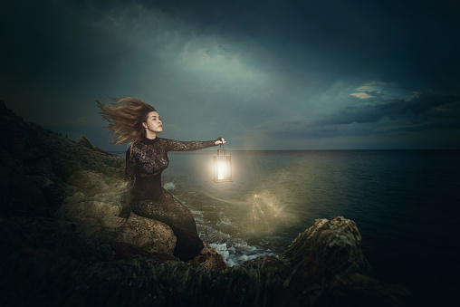 side view of young woman searching for the light,at the edge of the sea side in dramatic night.
