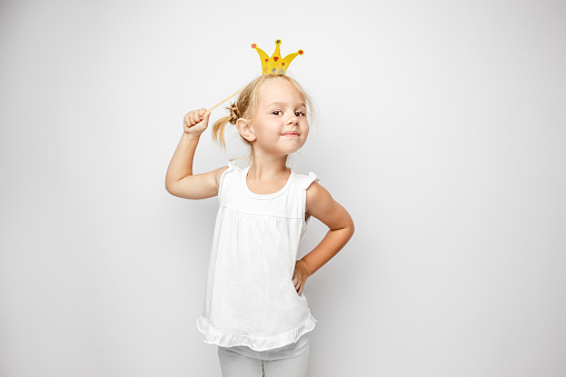 Beautiful little girl with paper crown posing on white background at home