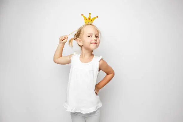 Beautiful little girl with paper crown posing on white background at home