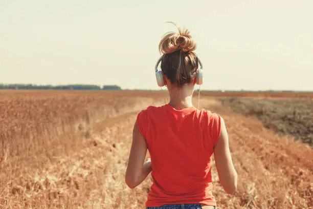 The girl in earphones in the field of wheat, in a red t-shirt listens to music