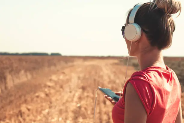 The girl in earphones and the smartphone in a hand, listens to music in the field of wheat