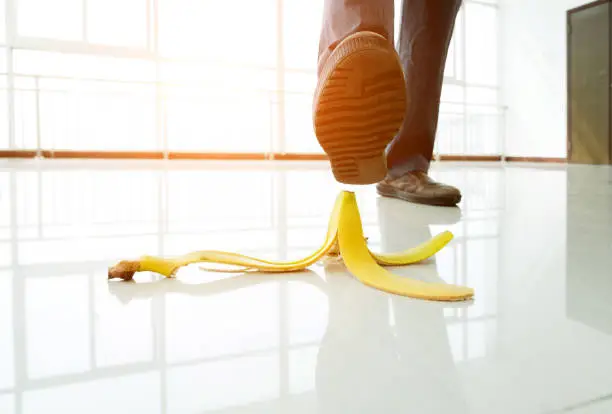 Businessman stepping on banana skin in office building hall.
