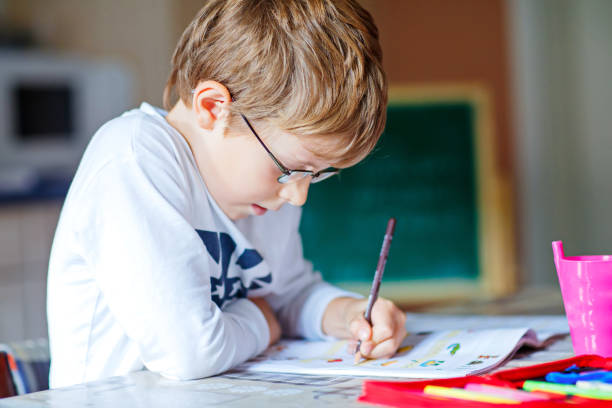 istock Happy school kid boy with glasses at home making homework 841837650