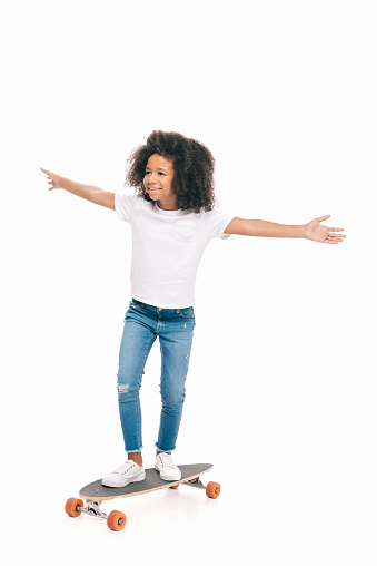 happy african american girl with open arms standing on skateboard isolated on white