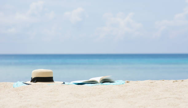 istock Summer hat and open book on sarong at beach. 841877550