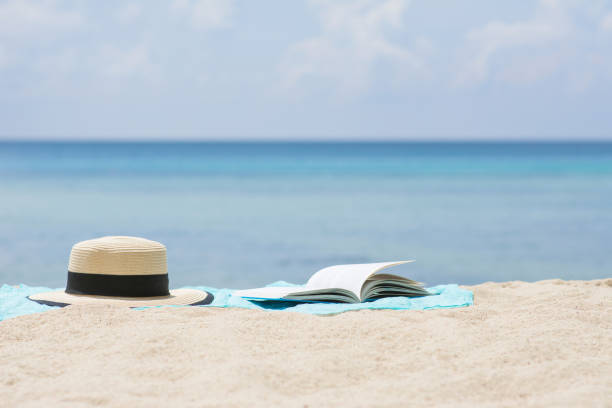 istock Open book and Summer hat on sarong at beach. 841877726