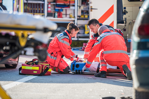 Injured man on patient transport stretcher. Ambulance staff member assisting injured person with transport stretcher. Paramedics assisting injured person first aid on road