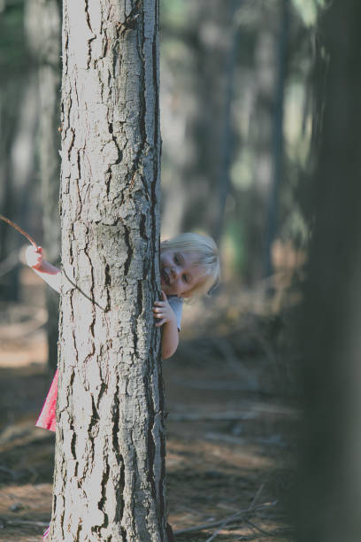 istock A blond girl hides behind a tree in the forest 841905066
