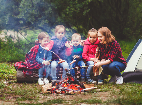 Happy tourist family on a journey hike. mother and children fry sausages on bonfire near the tent