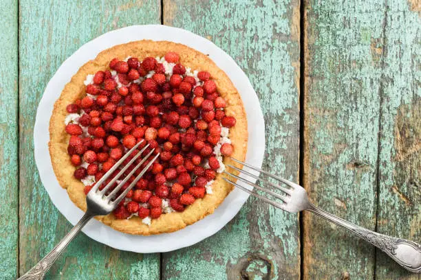Homemade tart with fresh forest strawberries and cottage cheese served with vintage forks overhead view