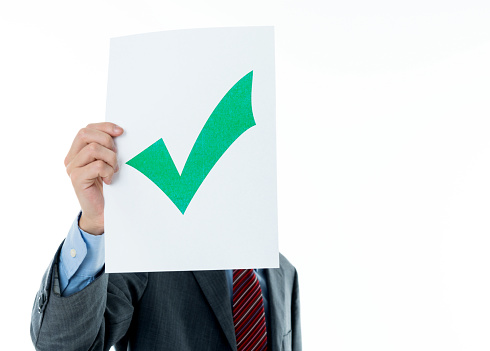 Young businessman holding a check mark against white background.