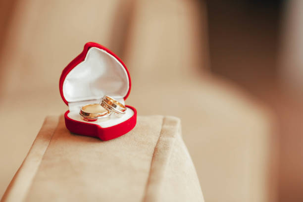 istock Two golden wedding rings with diamonds in a red heart-shaped box with on light background. Artwork. Soft focus 841954500
