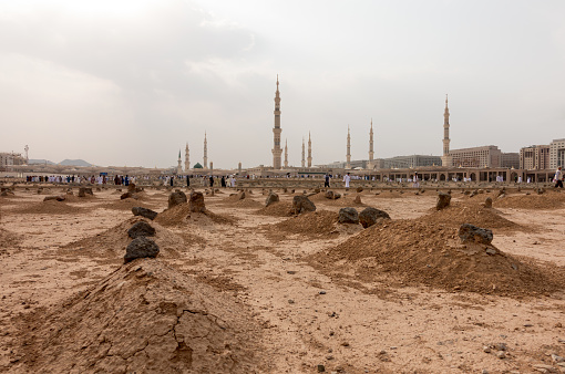 Ancient graves in Jannat Al Baqi Cemetery and the Prophet's Mosque al Masjid an Nabawi at the background in Medina, Saudi Arabia