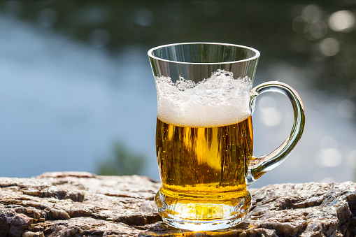 Mug of beer is stand on the rock above the river