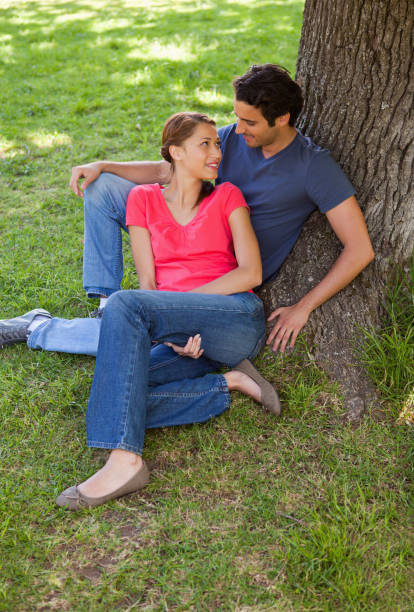 istock Two friends looking at each other while sitting together against a tree 841991814