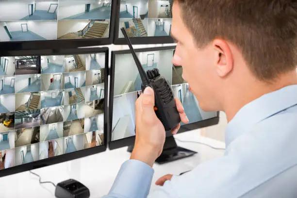 Close-up Of Male Security Guard Talking On Walkie-talkie While Monitoring Multiple CCTV Footage
