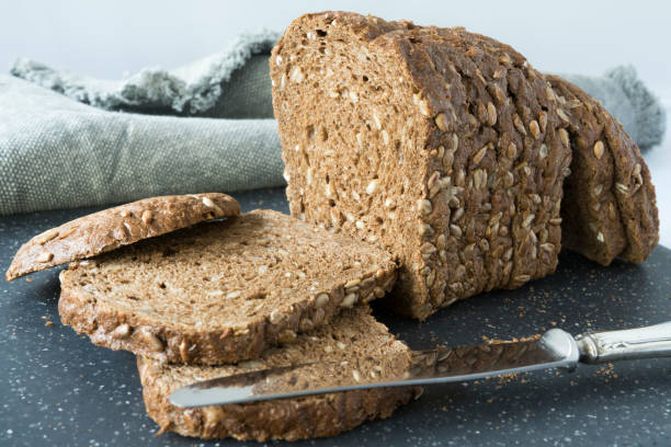 tranches de pain brun à grains entiers avec des graines de tournesol, sur une planche à découper gris - brown bread bread wheat bakery photos et images de collection