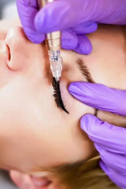 Photo of Woman having permanent makeup on eyeliner in beautician salon