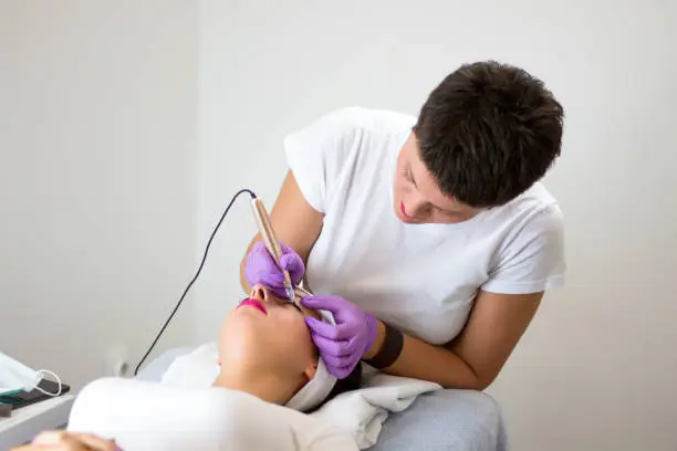 Photo of Professional Beautician applying permanent make up eyeliner on girl in beauty studio