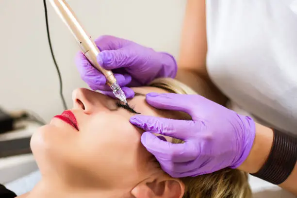 Photo of Professional Beautician applying permanent make up eyeliner in beauty studio