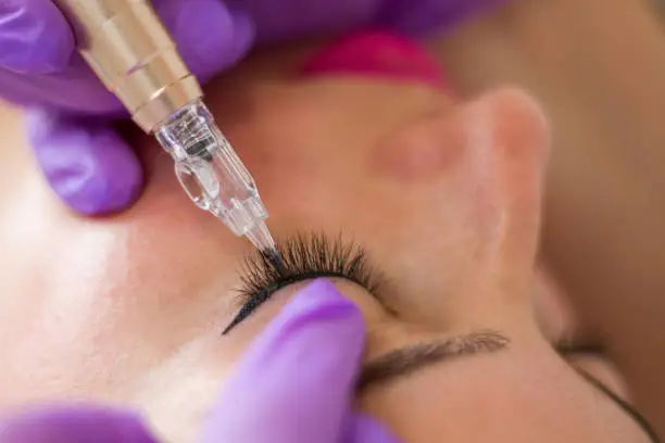 Photo of Young woman having permanent makeup on eyeliner in beautician salon