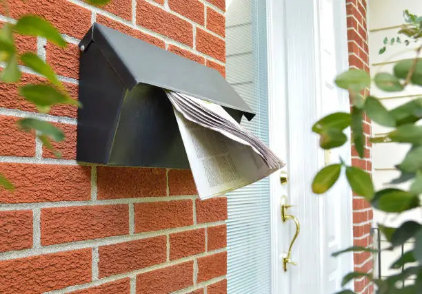 A letter box with a newspaper, next to the front door of a home.