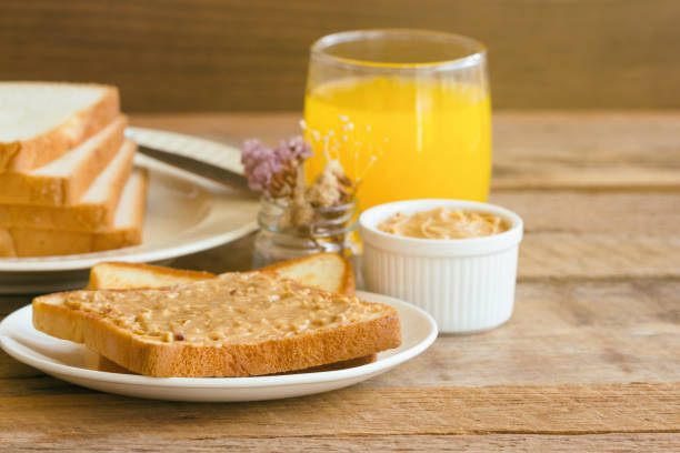 Toast bread with homemade peanut butter served with orange juice. Homemade toast bread with peanut butter on wood table for breakfast.Delicious toast bread with homemade peanut butter ready to served.