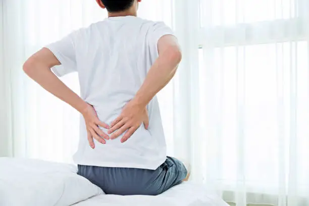 Young man sitting on the bed suffering from backpain.