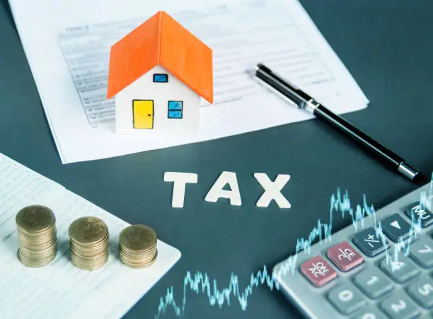 Tax words written on table with calculator,pen, miniature house with money and tax papers.
