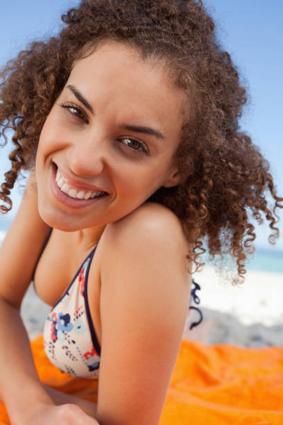 istock Young smiling woman lying down on a beach towel while staring at the camera 842101038