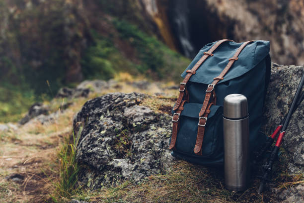 Hipster Blue Backpack, Thermos And Trekking Poles Closeup, Front View. Tourist Traveler Bag On Rocks Background. Adventure Hiking Outdoor Concept stock photo