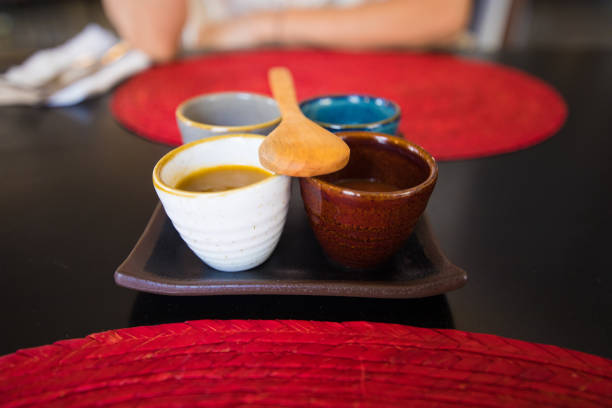 brown ceramic tray with four colorful bowls with sauces and wooden spoon on black table with red straw place mats
