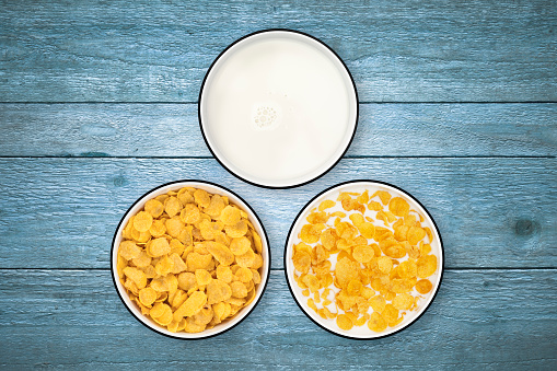 Milk and cornflakes in three circle bowls on a rustic old wood background, shot from directly above.