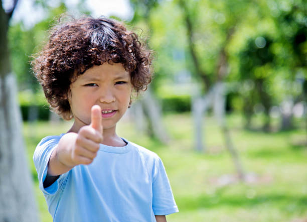 heureux petit garçon avec le pouce vers le haut à l’extérieur - hand sign human hand ok sign grass photos et images de collection