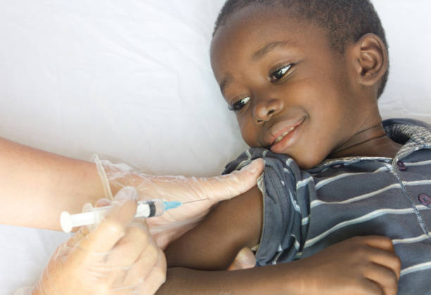 Happy African child gets a needle injection from a white volunteer Doctor stock photo