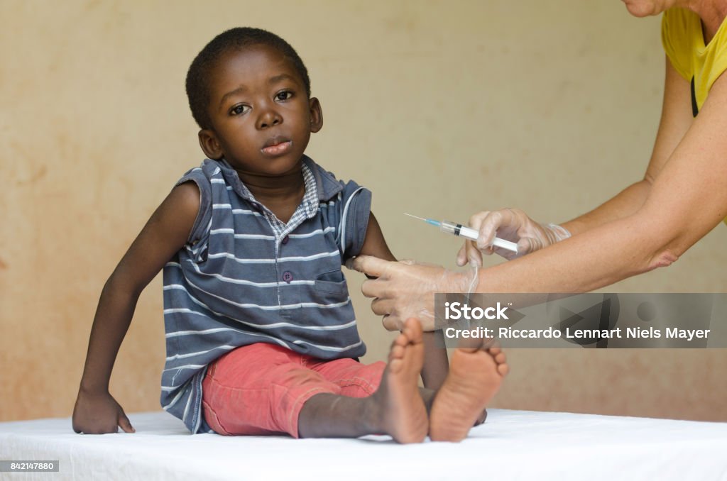 Sad African boy ready to get an injection from a volunteer nurse in Bamako, Mali A nice close-up of a little black African ethnicity boy getting a medical injection as a vaccination. Symbol for African illness fighting. Black boy as a patient for a white woman nurse. Child Stock Photo
