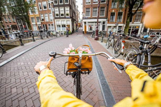 Riding a bicycle in Amsterdam Woman riding a bicycle with bouquet of flowers on the street in Amsterdam city. View on the hands holding helm amsterdam stock pictures, royalty-free photos & images
